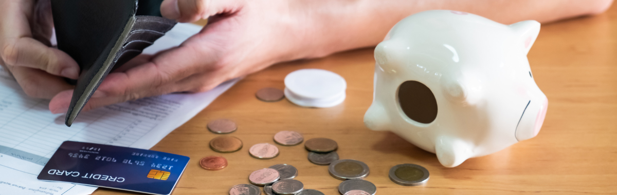 empty wallet, credit card, and piggy bank opened with coins spread across a table