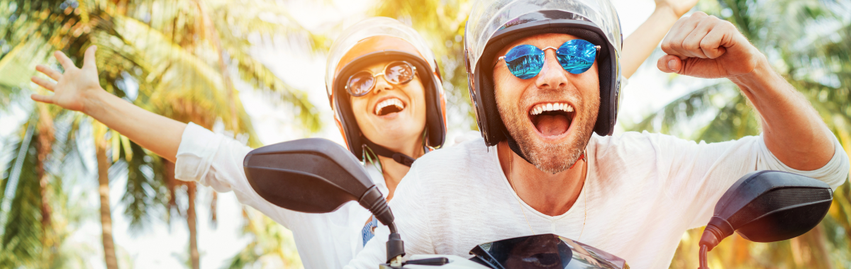 couple on a moped wearing helmets and sunglasses excitedly cheering