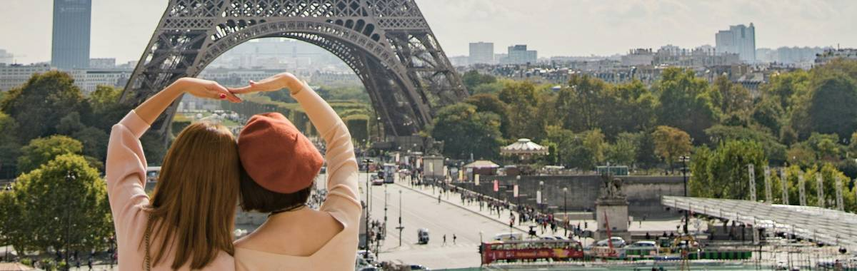 couple making a heart while infront of the eiffle tower