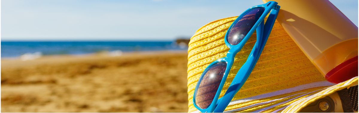 hat, sunglasses, and sunscreen sitting on a beach