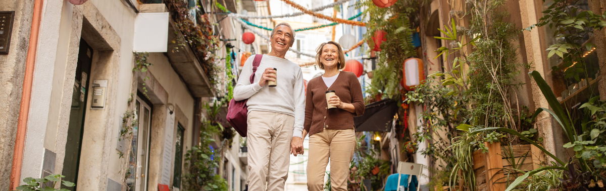 senior couple walking down street with coffee while smiling