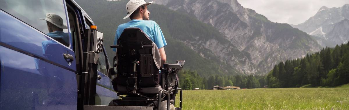 man sitting in a wheel chair outside a van in the mountains