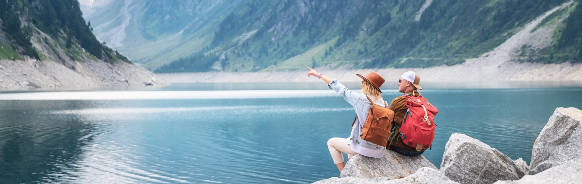 couple sitting on a rock next to a lake pointing at something in the distance