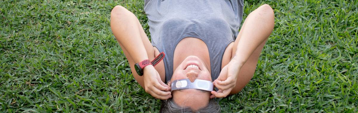 woman laying in the grass with eclipse glasses looking up at the sky