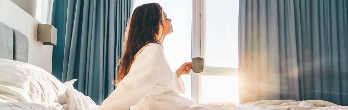 woman waking up in her hotel bed with a cup of coffee