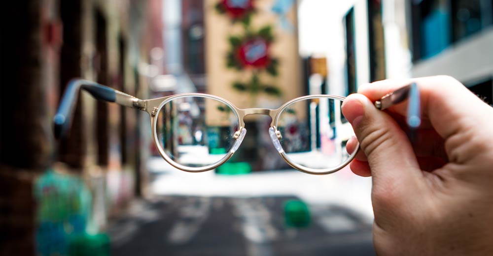 eyeglasses held in hand with city in background