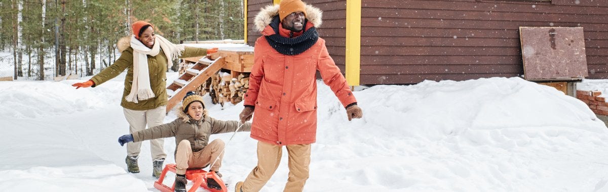 family playing in snow as father pulls sled with kid on it 