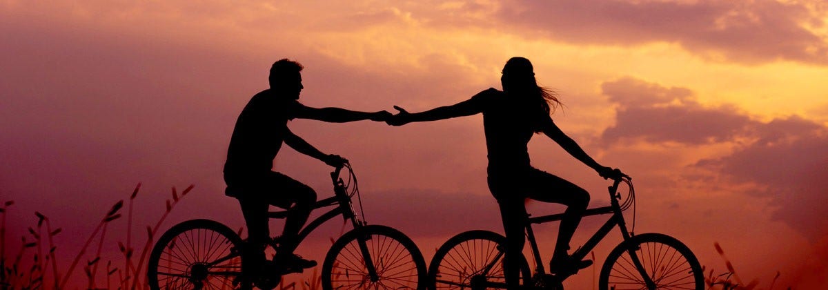 couple holding hands on bikes at sunset