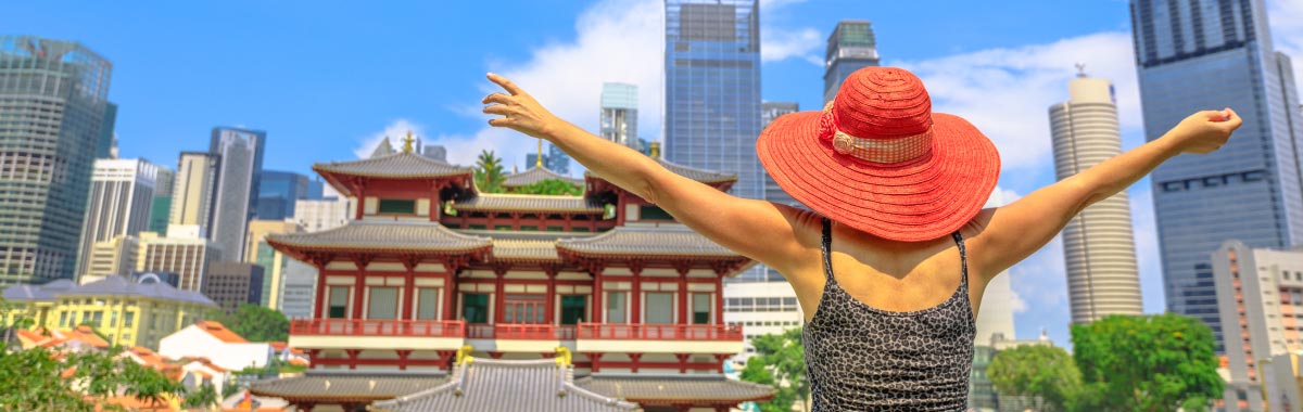 woman on a trip to Singapore with a pagoda style building in the foreground and cityscape in the background