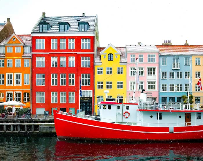 Old Boat harbored in one of Copenhagens harbors with a series of colorful red and yellow buildings behind it