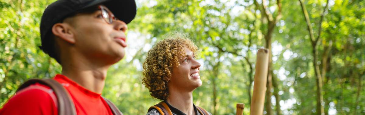 two guys in a forest looking up and smiling
