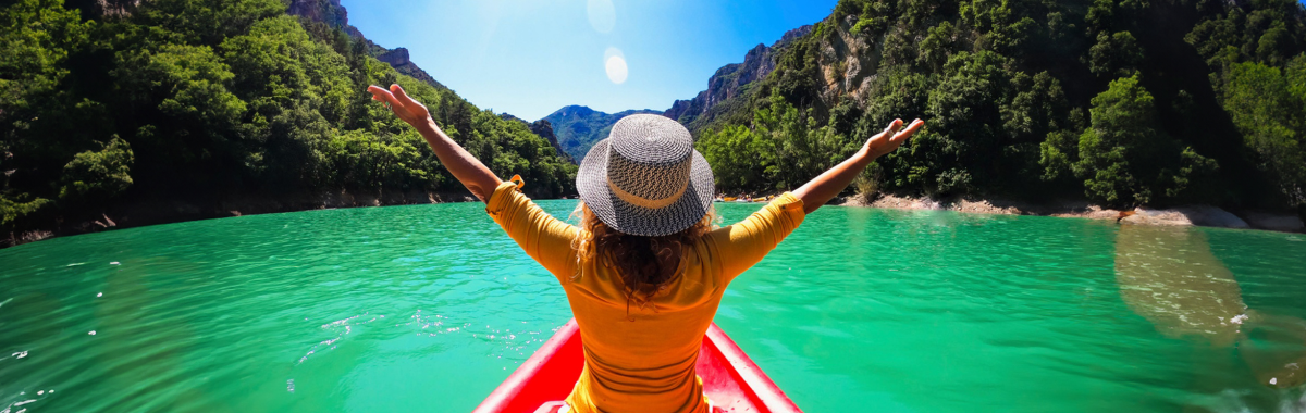 woman on a kayak with her arms out stretched over a emerald green lake