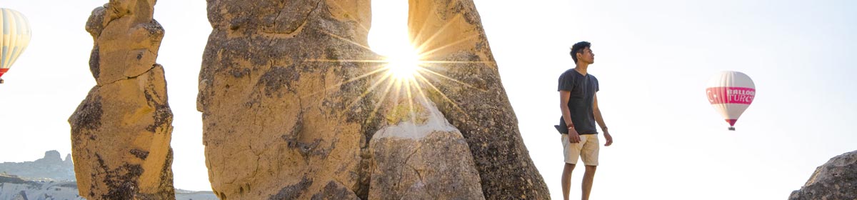 man standing on rocks looking at hot air balloon