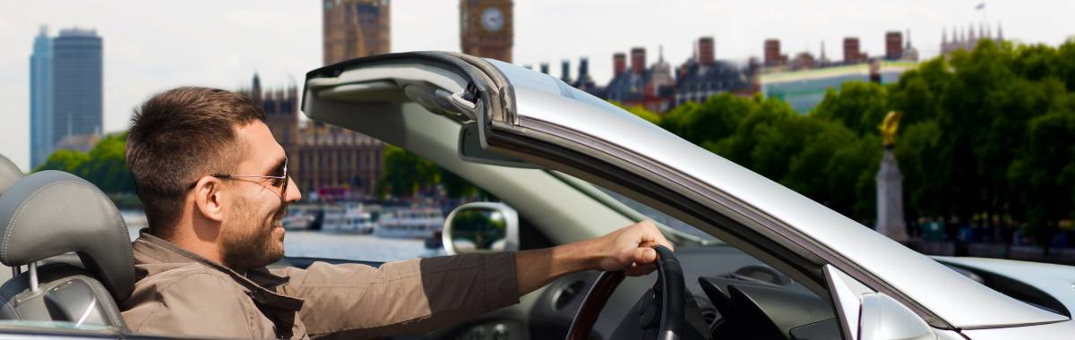 man driving with the top down in his car 