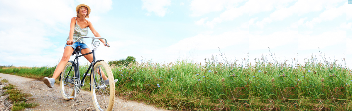 Header image of a happy woman on a bicycle traveling down a path in a field, looks like she has peace of mind 