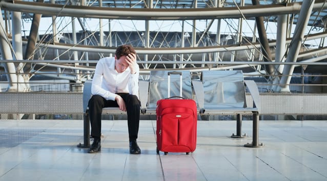 man with red suitcase, sitting on a bench, head in hands, airport, bus train station