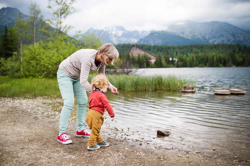 toddler and woman playing on the shore of a lake
