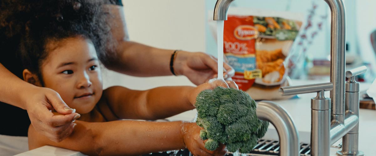 girl washing broccoli in the sink with her mom