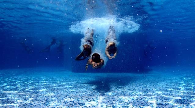 three people diving into a pool