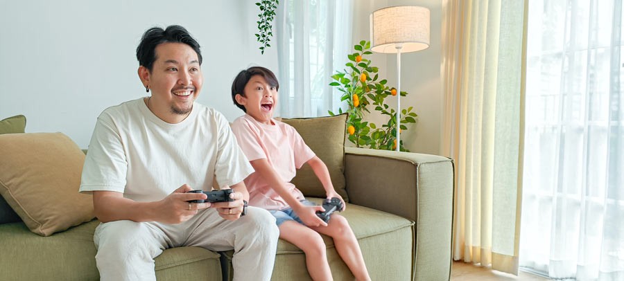 father and son playing video games on a couch having fun