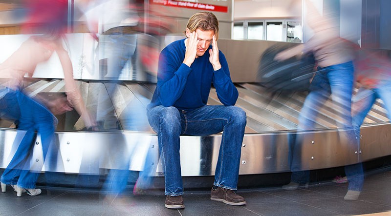man sitting on a baggage claim carousel looking stressed