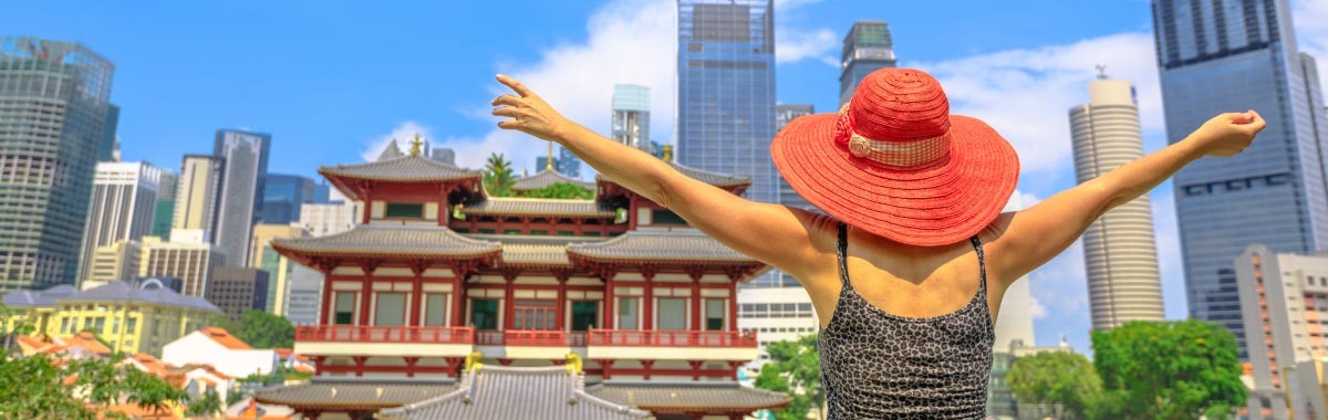 woman on a trip to Singapore with a pagoda style building in the foreground and cityscape in the background