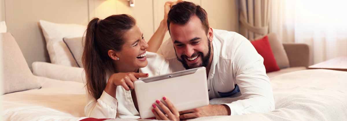 happy couple on a hotel or vacation rental bed with a tablet