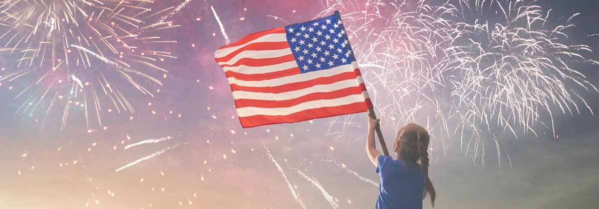 Girl at july 4th event, holding American Flag with fireworks in background