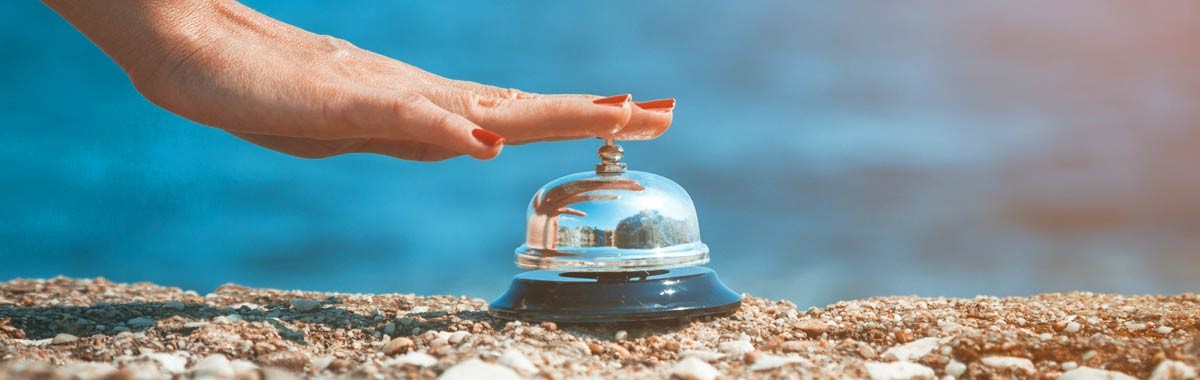 hand ringing concierge bell on a beach