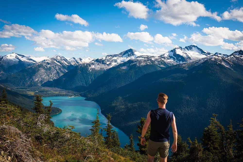 man looking at view of mountains, lake and forest in Whistler, Canada